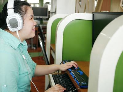A woman using a computer with headphones and a Braille display, representing digital accessibility and inclusive technology.