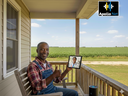 AI-generated image of a smiling farmer on a wooden porch holding a tablet showing a doctor on screen, symbolizing reliable telehealth access made possible by Apollo Net’s affordable rural internet service.