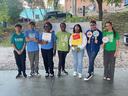 Seven young people standing in a row outdoors holding signs, some reading "VOTE".