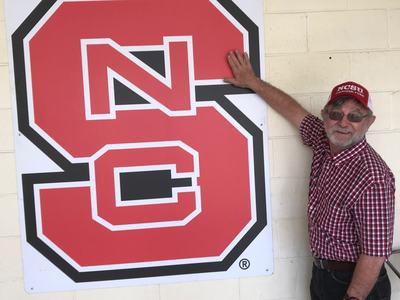 man standing and touching a NC State sign