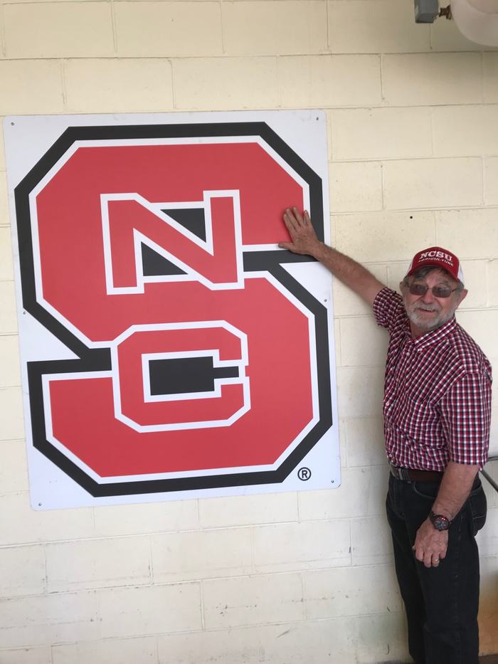 man standing and touching a NC State sign