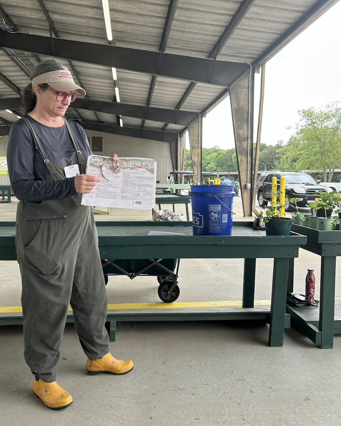 Woman in overalls pointing at a paper while standing by a covered market table