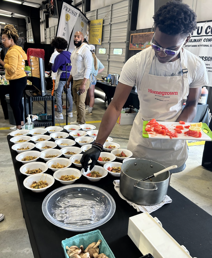 Person in "Homegrown" apron adding diced tomatoes to multiple food bowls on a serving table