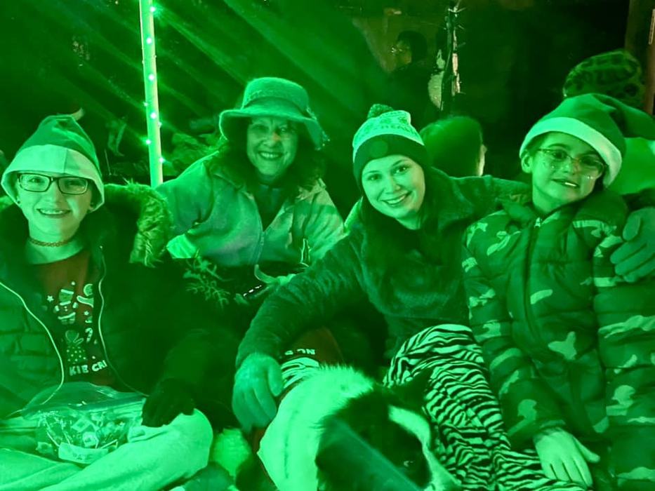 2 adults and 2 children bathed in green light on back of Christmas float