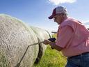 Man using drill to secure netting on large round hay bales in a grassy field