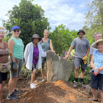 Group of adults standing around large rock.