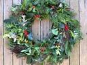 Wreath of mixed green foliage with red berries on wooden plank background