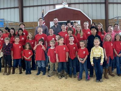 Large group of children and teens in barn arena, many wearing red shirts