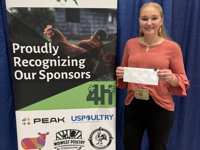 Photo of 4-Her Elizabeth Peluso in front of National 4-H Poultry and Egg Conference banner with her check and pin for winning reserve national champion at the egg chef challenge competition.