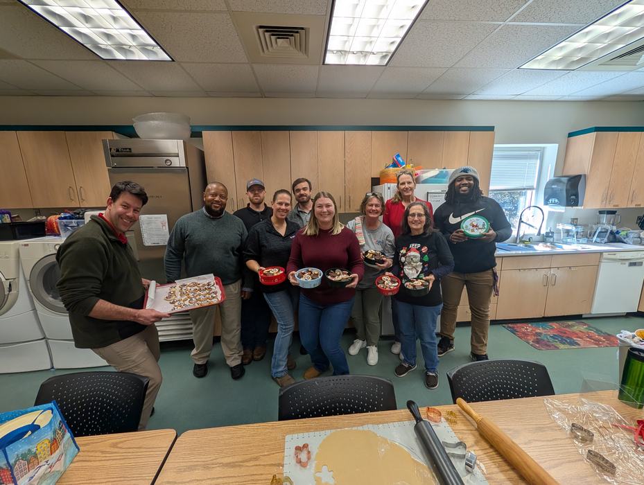 Group of people in a kitchen holding bowls and trays of decorated cookies.