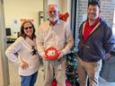 Three people standing by a small Christmas tree; center person holds red tin reading "Happy Holidays"