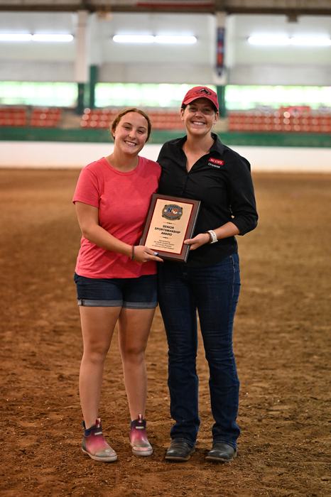 Two people standing in an arena holding a plaque reading "Senior Sportsmanship Award"