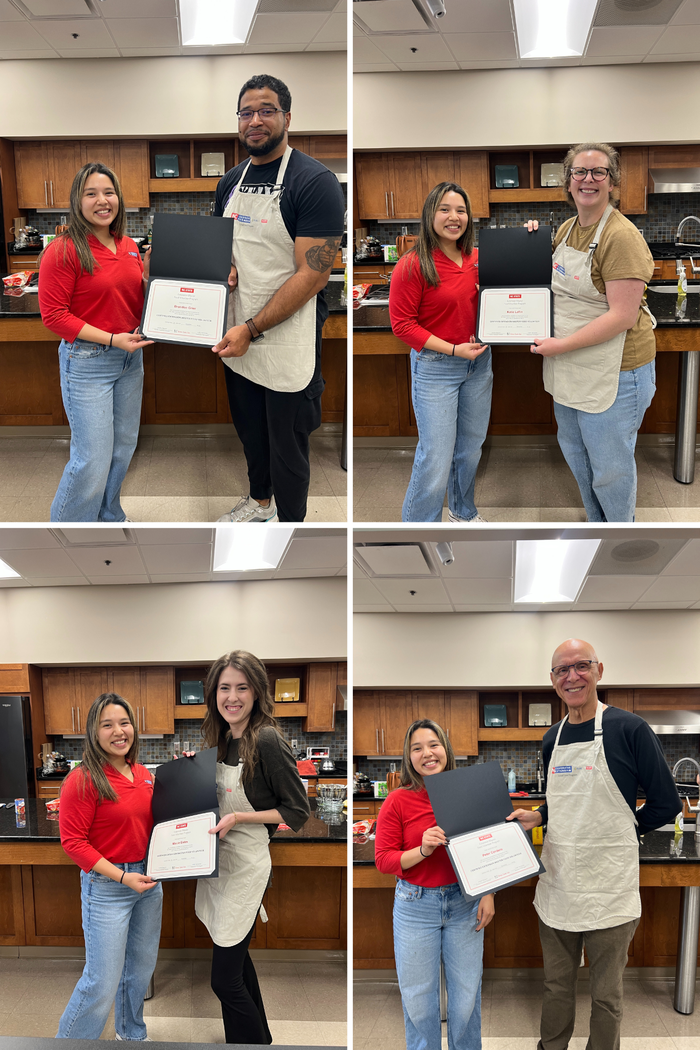 Woman in red handing framed certificates to four different people in a kitchen setting