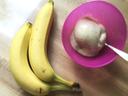 Image of 2 ripe bananas laying to the left of a pink bowl with a scoop of Banana Ice Cream and a spoon inside.
