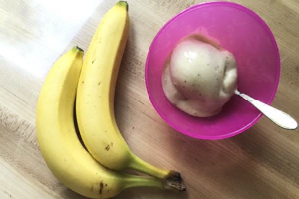 Image of 2 ripe bananas laying to the left of a pink bowl with a scoop of Banana Ice Cream and a spoon inside.