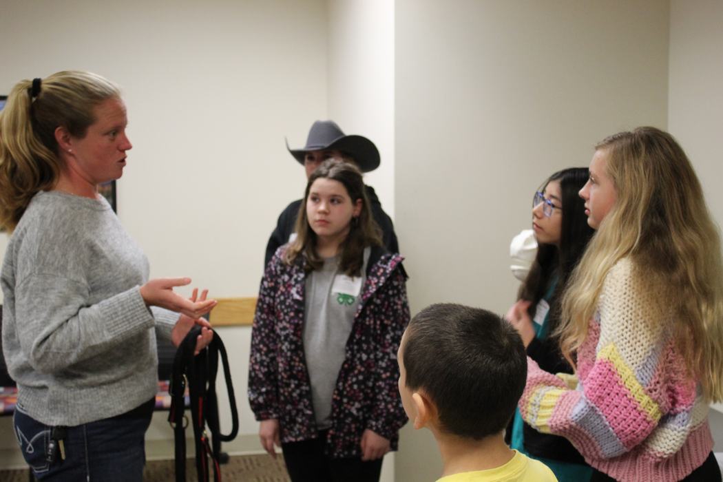 Adult woman speaking to a small group of children and teens indoors, holding straps.