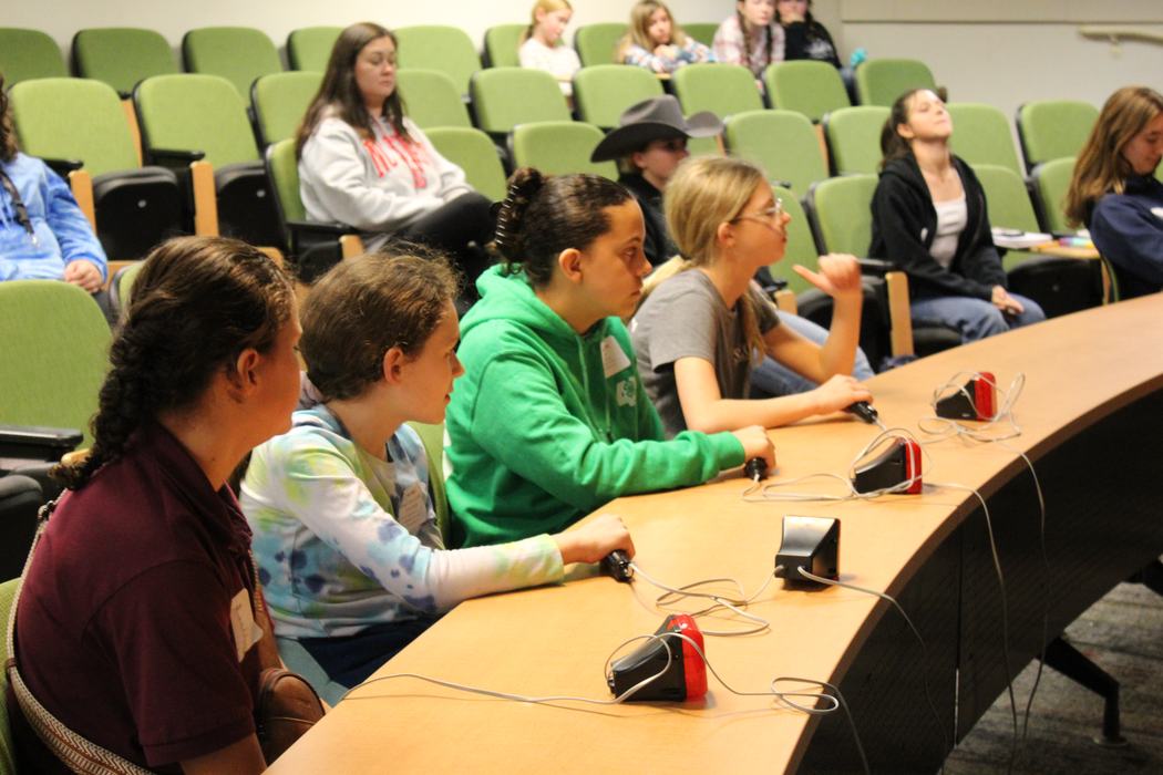 Students seated at a curved table holding handheld buzzers in a lecture hall