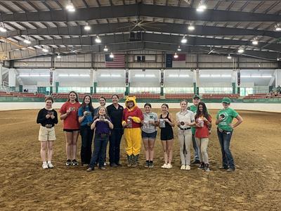 Teens and adults in indoor riding arena holding plaques and ribbons