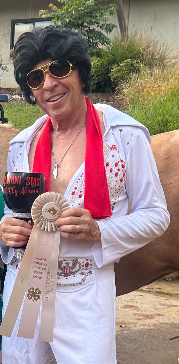 Person in Elvis costume holding trophy and ribbon reading "North Carolina State 4‑H Horse Show"