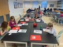Elementary students seated at tables coloring and working on worksheets in a classroom
