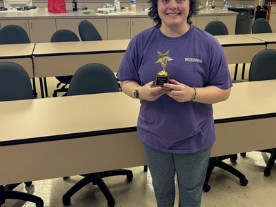 Image of Meredith Byers standing in kitchen holding her golden star award