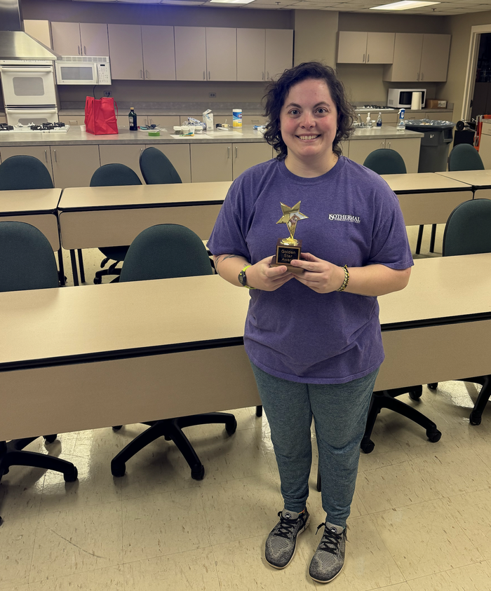 Image of Meredith Byers standing in kitchen holding her golden star award