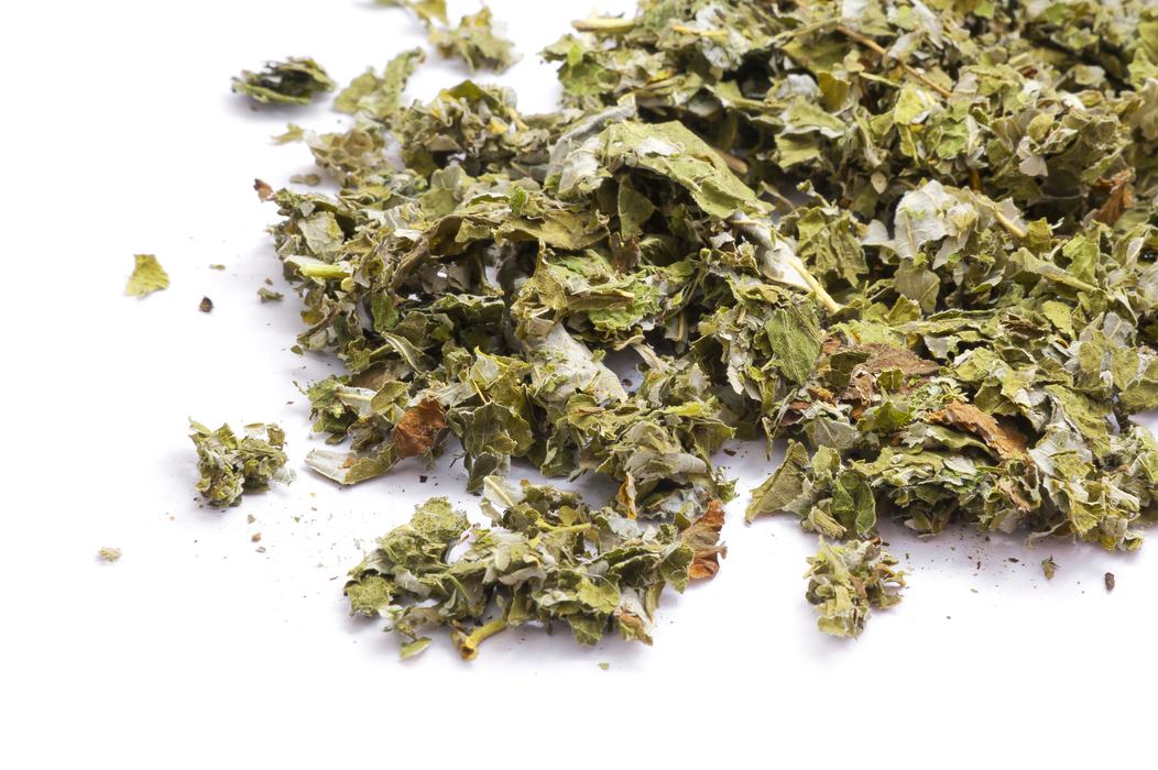 Loose dried green herb leaves scattered on a white surface.