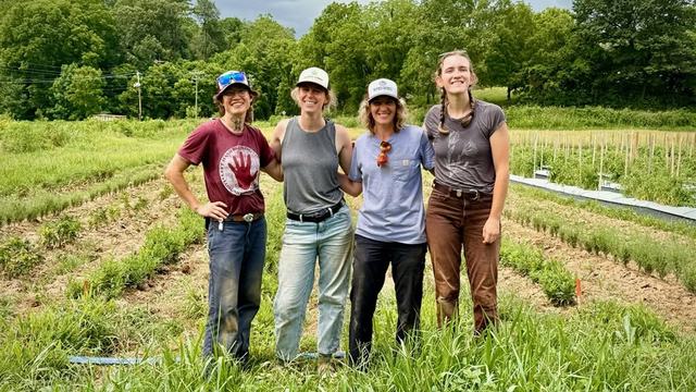 Four women in work clothes standing in front of a field of medicinal herbs