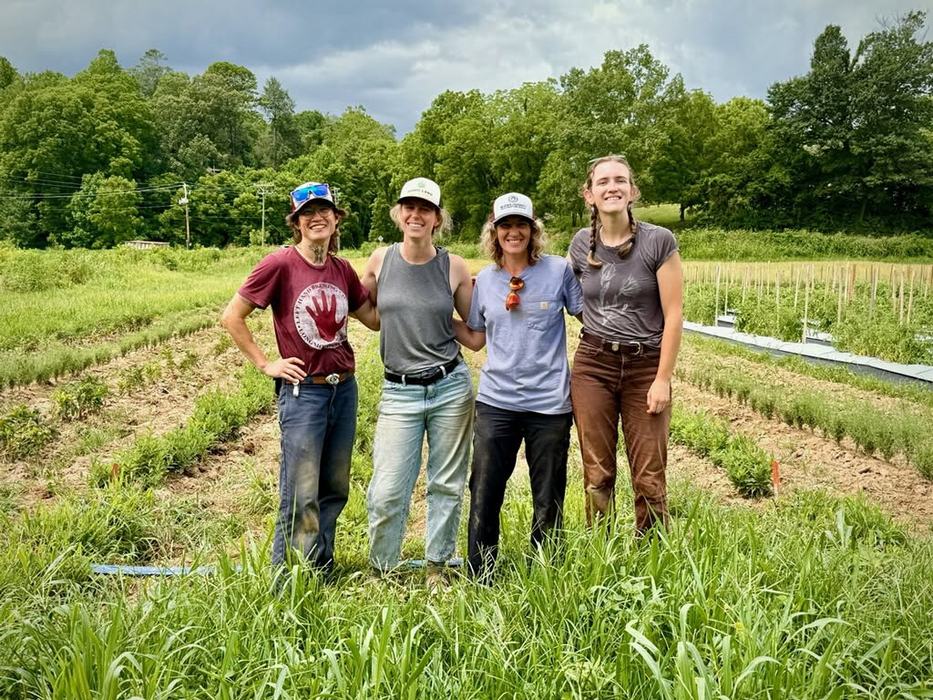 four women in work clothes standing in front of a field of medicinal herbs