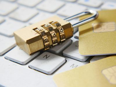 Close-up of a brass combination lock and two gold credit cards sitting on a white laptop keyboard.