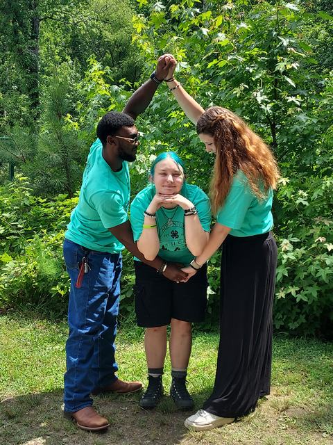 Three people in green shirts form an arch over a person wearing a 4‑H clover shirt