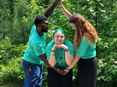 Three people in teal shirts forming an arch over a person standing with hands under chin