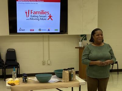 Woman by demo table with screen reading "Families Eating Smart and Moving More"