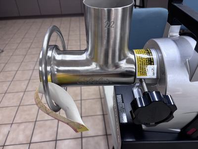 Stainless steel meat grinder head labeled "22" and "Cabela's" mounted on an electric grinder