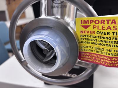 Meat grinder front with auger and plastic collar, tag reading "IMPORTANT PLEASE NEVER OVER-TIGHTEN"