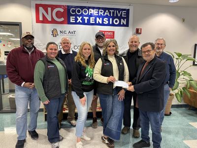 Group standing under NC Cooperative Extension banner handing over a check