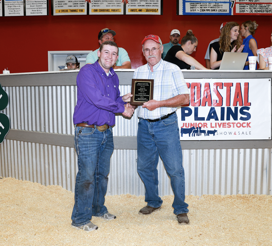 Two men shaking hands as older man holds plaque at Coastal Plains Junior Livestock event.