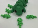 Green toy alligator with six smaller green toy alligators on a white surface