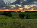 Sunset behind hills over rolling green fields with cloudy sky