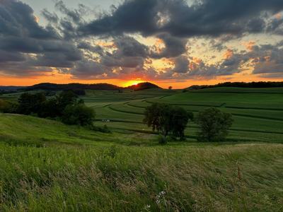 Sunset behind hills over rolling green fields with cloudy sky