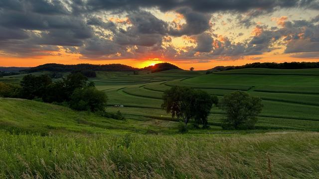 Sunset behind hills over rolling green fields with cloudy sky