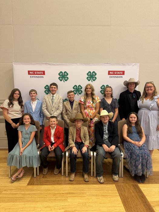 Group of youth posing before NC State Extension backdrop with 4‑H clover logos.