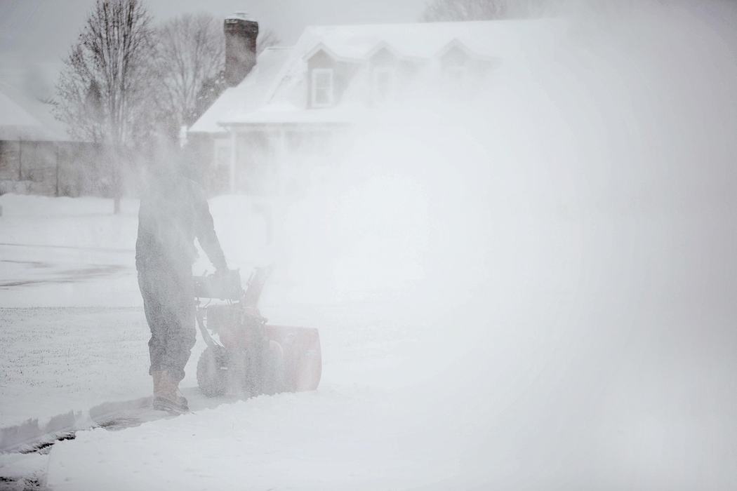 Person operating a snowblower clearing a driveway amid heavy blowing snow