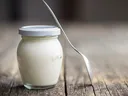 A Pot of yogurt with a spoon leaning on it.