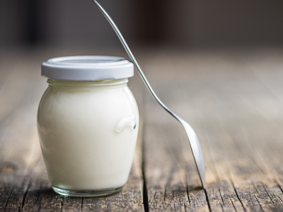 A Pot of yogurt with a spoon leaning on it.