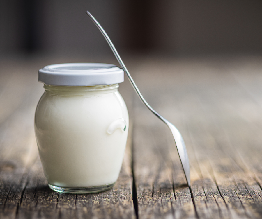 A Pot of yogurt with a spoon leaning on it.