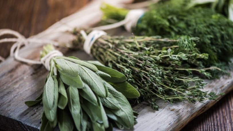 Three tied bundles of fresh herbs (sage, thyme, dill) on a wooden board.