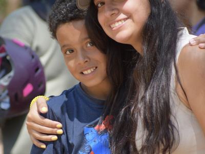 Young woman in cap with sunglasses hugs smiling boy outdoors