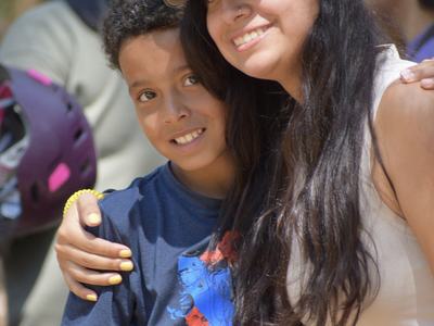 Young woman in cap with sunglasses hugs smiling boy outdoors