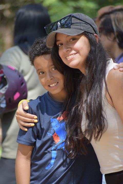 Young woman in cap with sunglasses hugs smiling boy outdoors